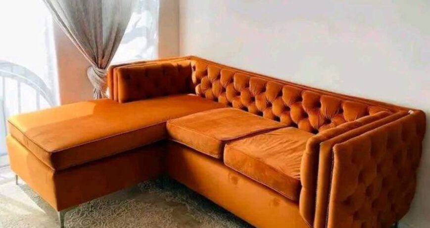Elevate your living room aesthetics with the Aura Velvet Chesterfield Sectional Sofa. Blending classic British elegance with modern functionality, this premium L-shaped sectional features deep button tufting, plush burnt orange velvet upholstery, and a sleek extended chaise lounge designed for ultimate relaxation and sophisticated entertaining.