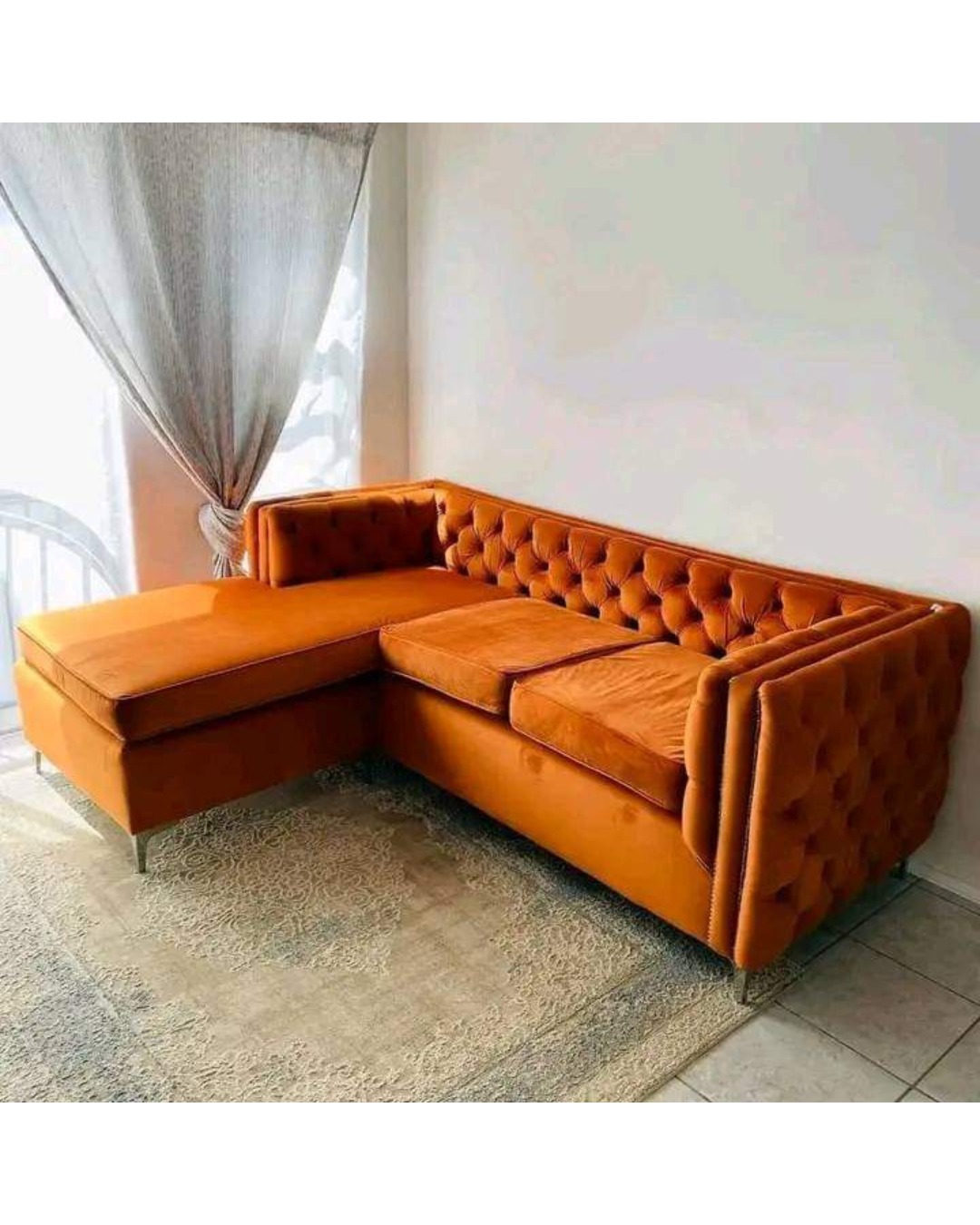 Elevate your living room aesthetics with the Aura Velvet Chesterfield Sectional Sofa. Blending classic British elegance with modern functionality, this premium L-shaped sectional features deep button tufting, plush burnt orange velvet upholstery, and a sleek extended chaise lounge designed for ultimate relaxation and sophisticated entertaining.